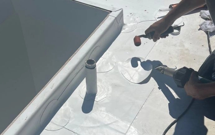 Technician using heat welding equipment to perform flat roof repair on a membrane roofing system.