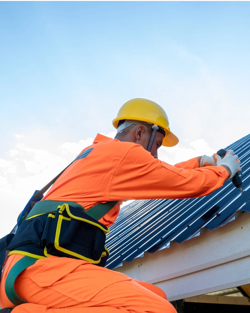 A roofing contractor wearing safety gear installing a metal roof under a clear blue sky in Fort Worth, Texas.